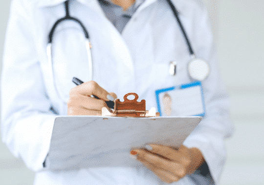 Female doctor with a stethoscope around her neck filling in a form on a clipboard - health insurance for expats