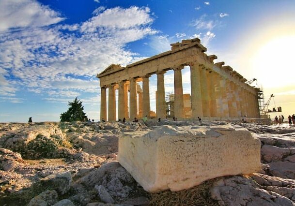 The Parthenon in Athens, Greece, with a bright sky and ancient stones around it. 