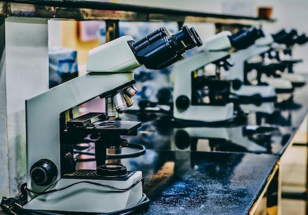 Row of microscopes lined up on a black laboratory table in a science classroom or lab.