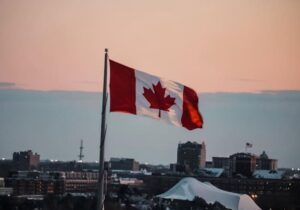 Canadian flag waving with buildings and the ocean in the background - living in Canada