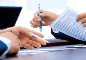 Two pairs of hands with pens reviewing documents about moving to Serbia