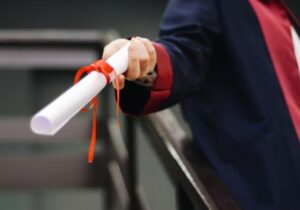 A person graduating holding a certificate wrapped in a red bow. 