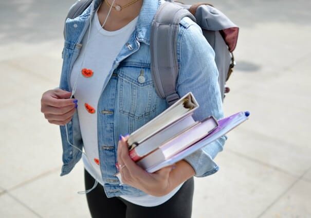 Woman with a denim jacket, walking with books and a backpack - education benefits of having second citizenship