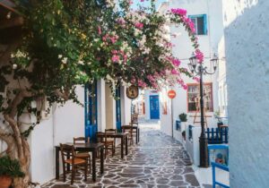 A walk way between white building with chairs and tables outside and beautiful pink flowers. 