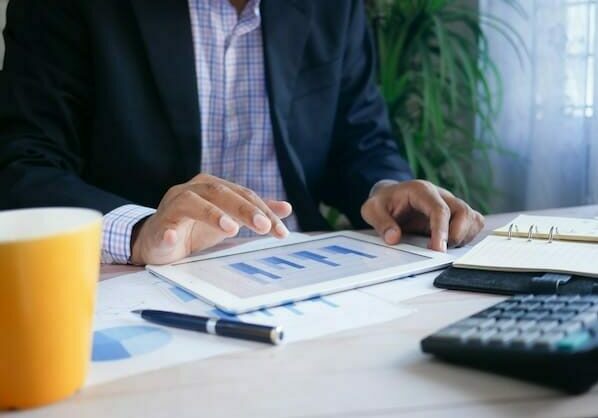 Man working on a table that's displaying a graph with a calculator and cup of coffee in front of him - country of tax residency