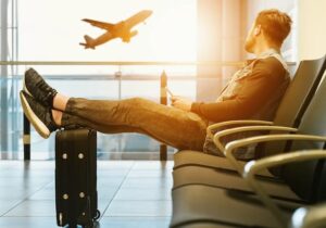 Man with his legs propped up on a suitcase while watching a plane depart in an airport - Schengen Business Visa