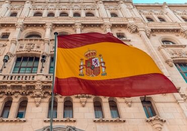 View of a Spanish flag and an old-fashioned building from below - best European residences for business owners