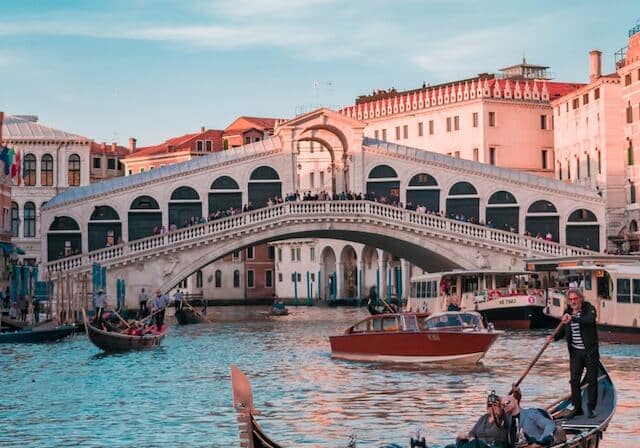 A building with a bridge over a canal, with boats floating below in aN Italian city.