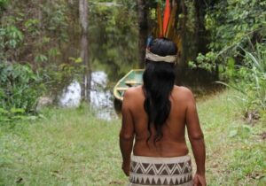 a Kalinago person walking toward a boat on a river
