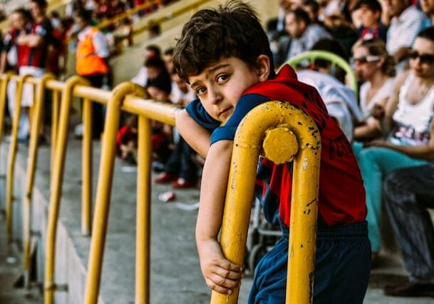 A child leaning against a rail with a crowd of people in the background. 