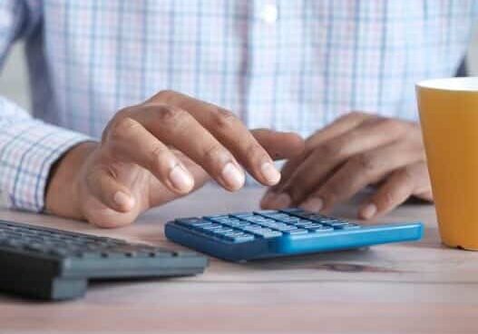 Man sitting at a desk working on a calculator and computer with a cup of coffee - countries that are tax havens