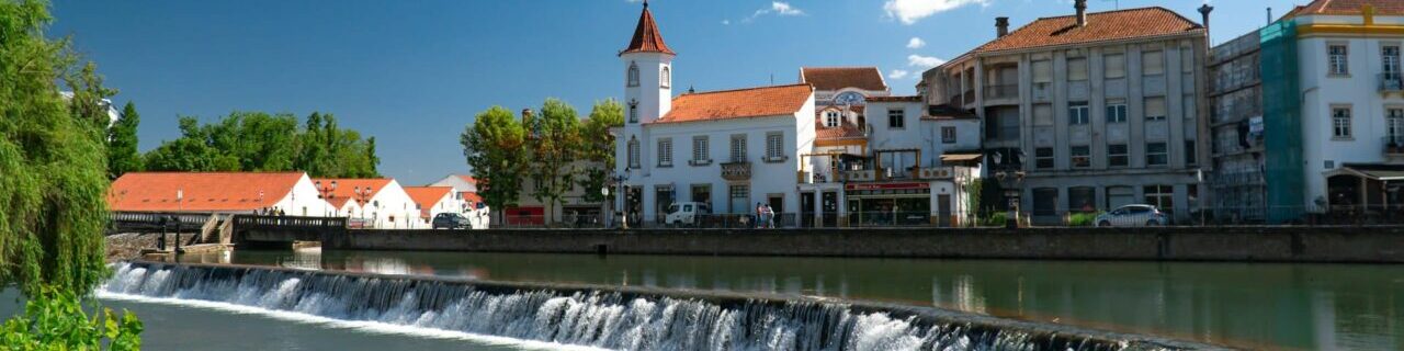 Cars parked along the river and buildings in Tomar, Santarem