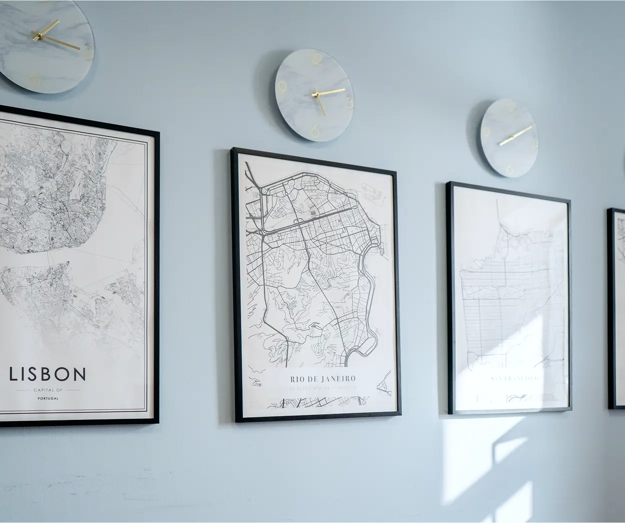 Three framed maps hang on a wall beside a round clock, creating a visually interesting and informative display.