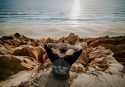 Man sitting on rocks on Melides beach in Portugal looking out over the ocean - best European countries to move to as a UK citizen