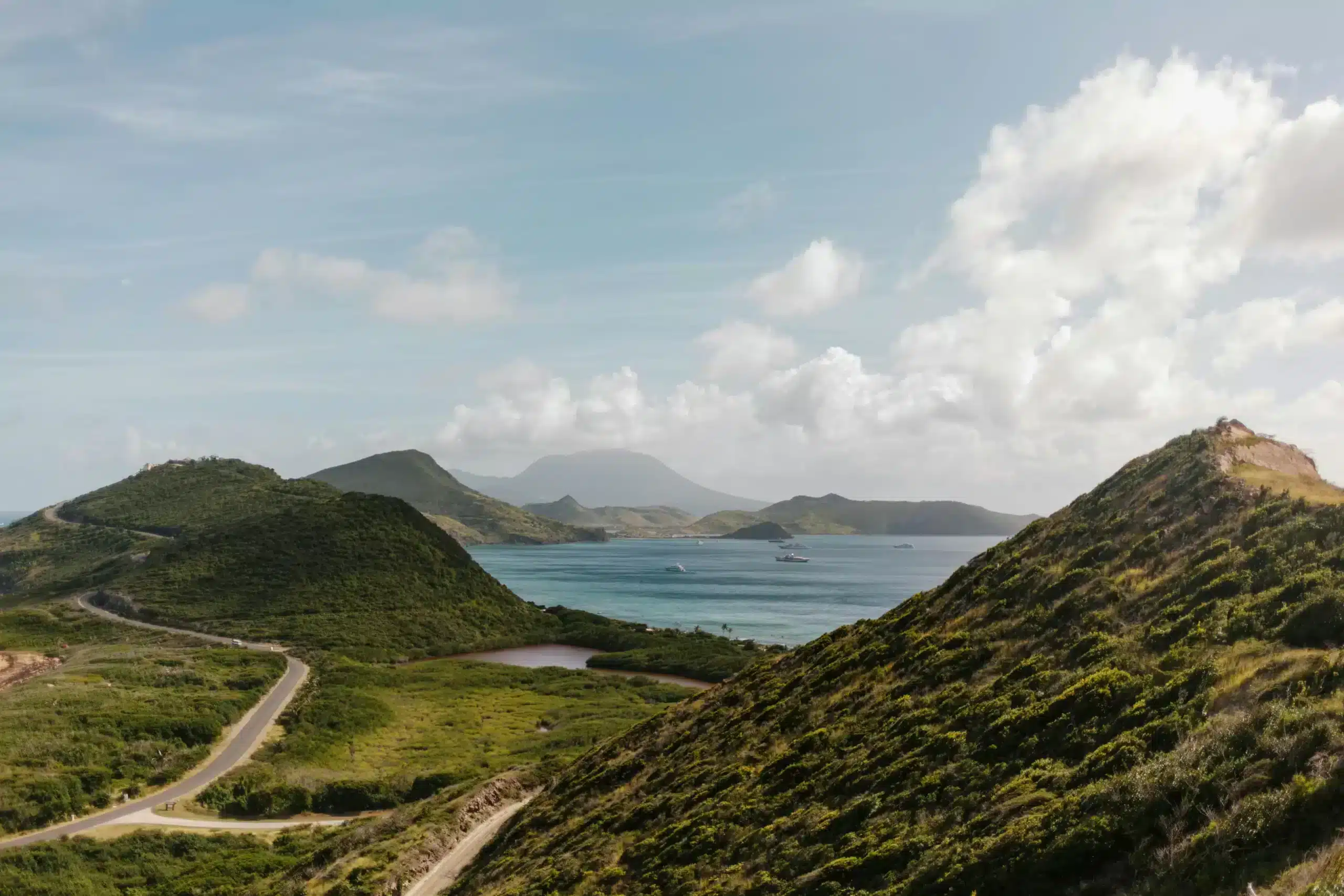 A scenic view of the ocean and mountains from a hill, showcasing vibrant blue waters and lush green peaks.