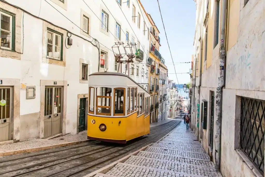 A yellow tram travels down a narrow street lined with buildings on either side.
