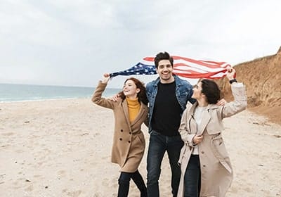 Three people walking on the beach, holding the US flag - permanent resident vs citizen